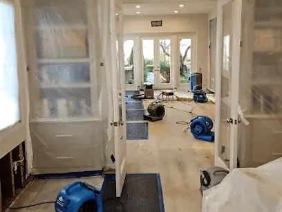 Air movers and a dehumidifier drying a hallway behind plastic containment sheeting