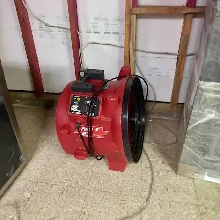 Red air mover beside an opened lower wall and plastic sheeting, equipment for an Oak Harbor water loss