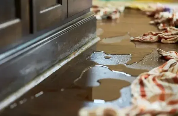 Water pooled along the base of a kitchen cabinet with towels laid down