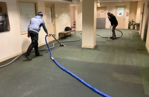 Two technicians extracting water from carpet in an office lobby